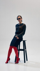 Elegant woman in black blouse, skirt, red tights, heels and sunglasses posing with confidence on...