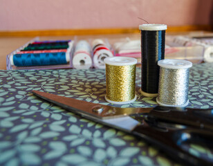 Reels of metalic thread, gold, silver and black on a green floral background with scissors