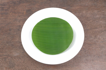 Ceramic plate with banana leaves in the plate on a wooden table, top view above.  Mockups can be used to edit food product displays or design layouts.