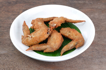 Fried chicken wings in a ceramic dish with banana leaves on a wooden table. Thai food.