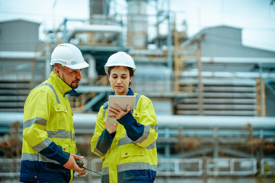 Engineers discuss project details while checking data on a tablet at an industrial plant