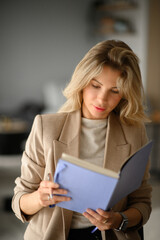 A beautiful businesswoman with white hair, wearing a beige blazer and holding a notebook, ready to make notes in a modern office setting, exuding elegance and professionalism