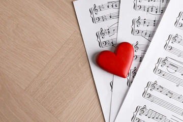 Heart figure and musical note sheets on wooden table, above view. Space for text