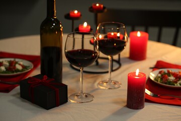 Red wine, burning candles and gift box on table. Romantic dinner