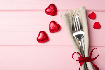 Romantic place setting for Valentine's day. Cutlery, napkin and decorative hearts on pink wooden table, flat lay. Space for text