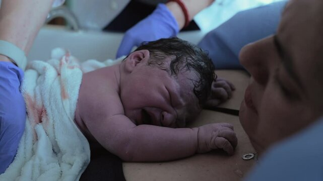 First seconds of life of a newborn baby right after birth struggling to take his first breaths of life resting on mother's chest emphasizing skin to skin contact, first cries of a human being