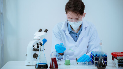Male scientist holding chemical test in science lab, blue glass tube in lab, holding liquid in glass tube, Asian male doctor working in medical chemistry.