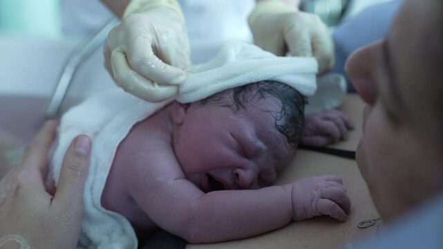Close-up of Newborn baby after birth, first seconds of life, nurse's hand putting warm clothes, initial minutes of life