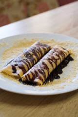 Two crepes drizzled with chocolate sauce and sprinkled with crumbs
