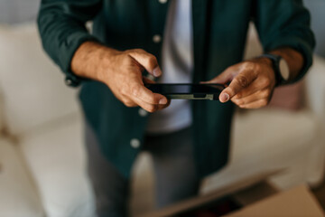 Mid-aged Caucasian man taking a photo of donation boxes with his smartphone in his living room