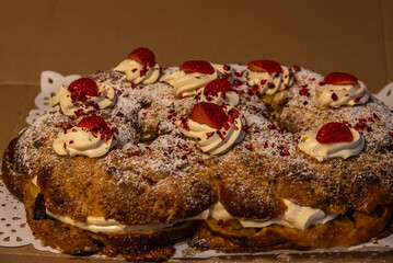 A delicious festive cake topped with whipped cream, fresh strawberries, powdered sugar, and crushed dried raspberries, displayed on a doily.