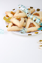 Close up freshly baked triangular cookies, adorned with light blue ribbons and decorated mask on a white table. Purim celebration concept. space for text