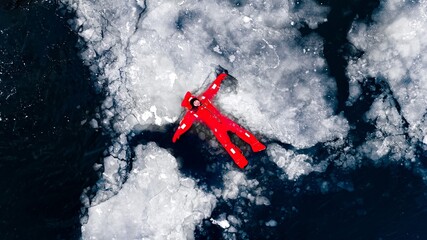 Aerial view of man ice floating on icy water in bright red survival suits. Arctic frozen landscape....