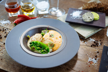 Scallops with shrimp foam, cauliflower cream and green peas on a plate. Delicious healthy seafood closeup served for lunch on a table in modern gourmet cuisine restaurant