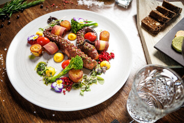 Octopus tentacles with cherry tomatoes, broccoli, and edible flowers. Accompanied by roasted potatoes, yellow sauce, and microgreens. Sophisticated seafood dish in a gourmet restaurant