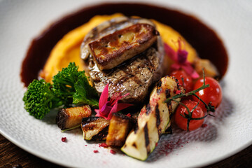 Succulent beef filet with foie gras, served with velvety mashed sweet potatoes, grilled zucchini, and cherry tomatoes. A gourmet meal in a sophisticated dining setting