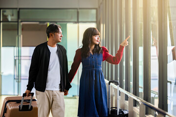 Happy smiling middle aged romantic couple pointing with finger at window in a modern airport terminal, gazing out at the view with a suitcase, Waiting for flight at terminal, Enjoying upcoming trip.