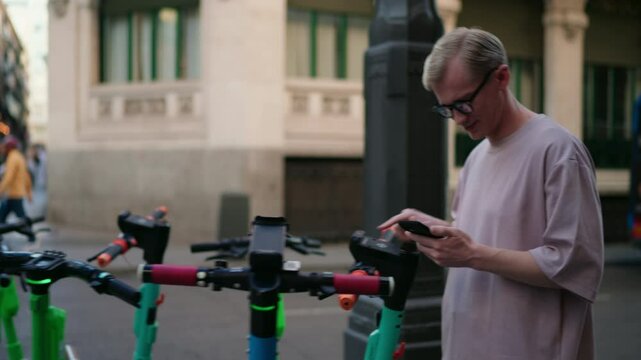Young man scanning QR code with smartphone app to unlock electric scooter sharing service on city street. Modern transportation, eco-friendly travel, and technology integration for urban mobility
