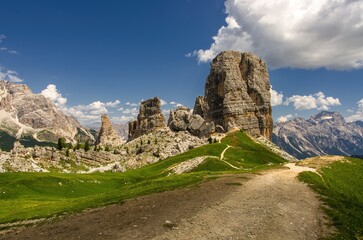 Obraz premium Majestic Cinque Torri in Dolomie Alps during day. Stunning view on Five Towers group, with blue sky and clouds and foot road. Amazing nature lanscape. Mountain trail leading along the mountain ridge.
