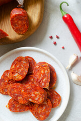 Slices of Spanish Chorizo sausage with red pepper, paprika and garlic on a small plate and ingredients. Traditional Mediterranean food concept. Vertical orientation. Selective focus. Top view