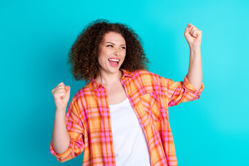 Burst of happiness expressed by a cheerful woman in a casual checkered shirt on teal background