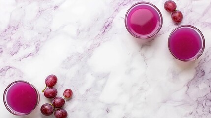Refreshing grape juice in small glasses alongside fresh grapes on marble surface