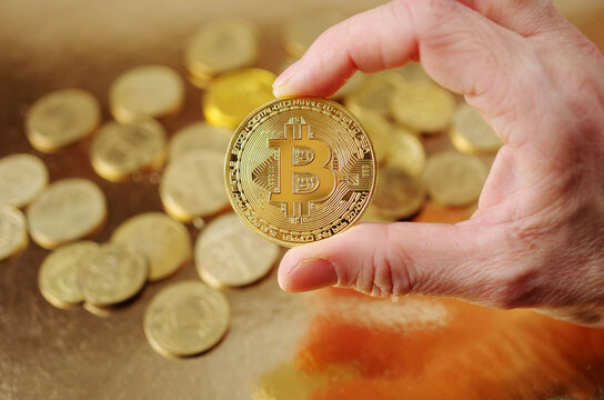 A hand holding a bitcoin coin against a background of scattered gold coins.
