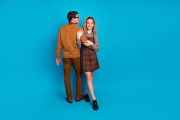 Young couple in retro style outfits posing on a vibrant blue background symbolizing friendship and casual fashion