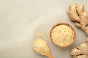 Ginger powder in bowl with fresh ginger root on light background. Top view