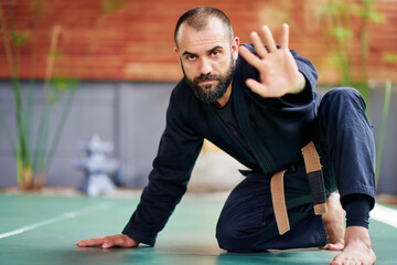 Martial artist practicing kata and showing stop sign with hand in dojo