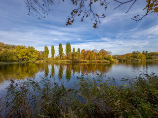 jesienny widok na kolorowe drzewa obrastające wokół jeziora z gładką spokojna taflą wody © Kamil_k2p