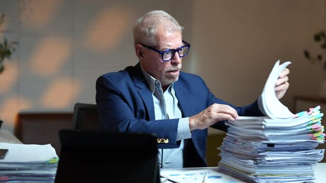Professional businessman experiencing intense work-related stress, hitting desk in exhaustion while overwhelmed by paperwork during late-night office hours