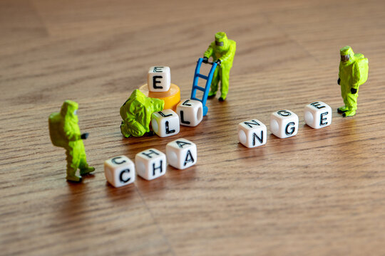 Naklejki Removing white cubes with letters l and e of the word challenge creating new word change on wooden background with miniature figurines in hazmat biohazard suites