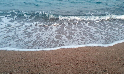 Clear transparent sea water and waves in sunny day with much sand and stones.