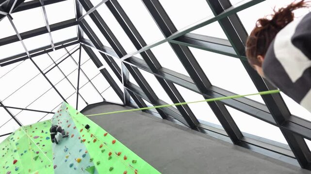 Couple climbing, the girl carefully belays the climber, her man, who is high up on the climbing wall.