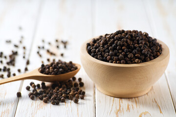 black pepper seeds in a wooden bowl on a white wooden table, selective focus.
