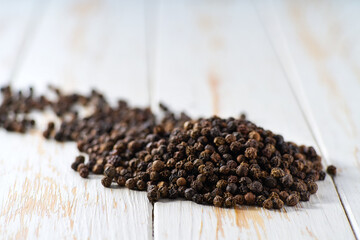Heap black pepper seeds on a white wooden table, selective focus.
