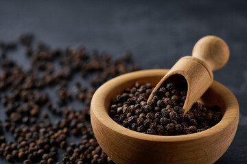 black pepper seeds in a wooden bowl on a black stone table, selective focus.
