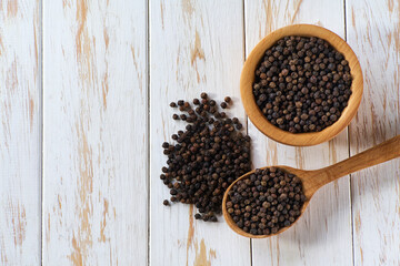 wooden bowl with black peppercorns on a light kitchen table, top view.