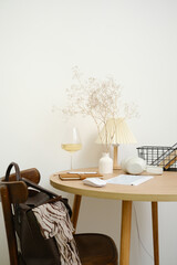 A calm and serene workspace showcasing a beautiful wooden table, stylish decorative elements, and a glass of fine wine, keyboard, books in a basket, headphones, bag on the shair.