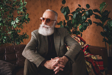 Elegant elder gentleman in stylish vintage attire seated indoors under warm retro lighting and surrounded by plants