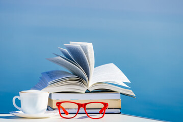 Coffee cup, book and glasses against blue sea.