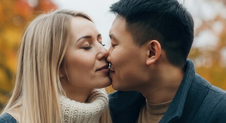 Naklejka premium Romantic autumn kiss between young caucasian female and asian male in a park setting