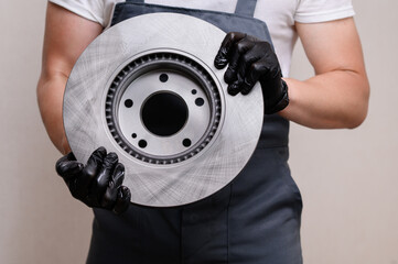 Male auto repairman holds new brake disc in hands, close-up. Auto parts replacement concept, car...