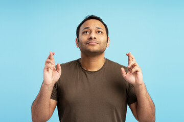 Hopeful man crossing fingers looking up wishing something on blue background