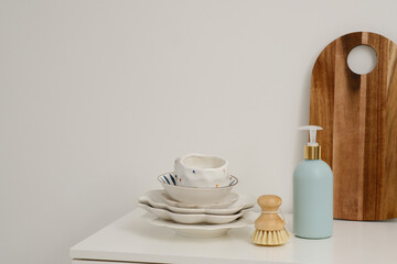  Bottle of dishwashing detergent with a natural brush and a stack of dishes on a minimalist white surface creates a perfect aesthetic
