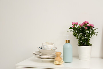  Bottle of dishwashing detergent with a natural brush and a stack of dishes on a minimalist white surface creates a perfect aesthetic