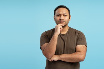 Pensive adult man touching chin and thinking on blue background