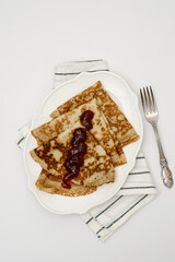 Sweet crepes assortment with berries jam on white background. Homemade food concept. Top view, flat lay