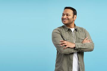 Confident indian man smiling and looking away on blue background